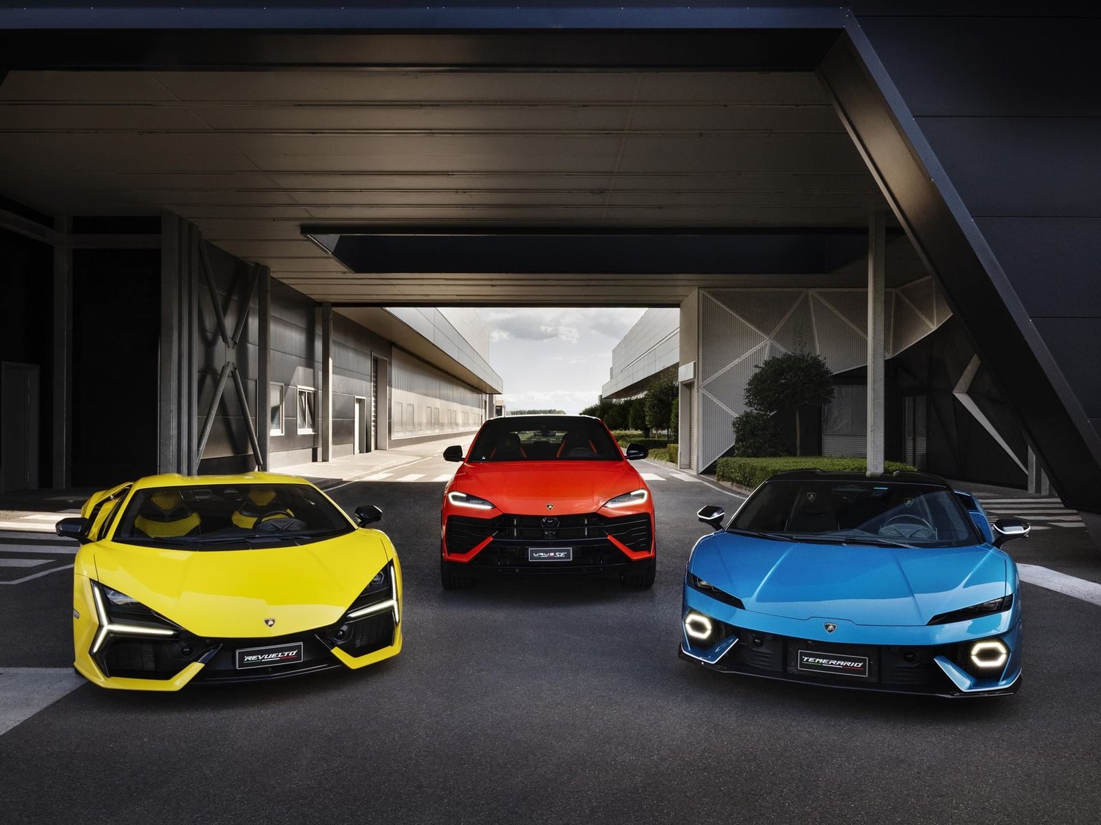 Lamborghini's fully hybrid lineup: a yellow Revuelto, red Urus, and blue Temerario parked together in a modern industrial setting