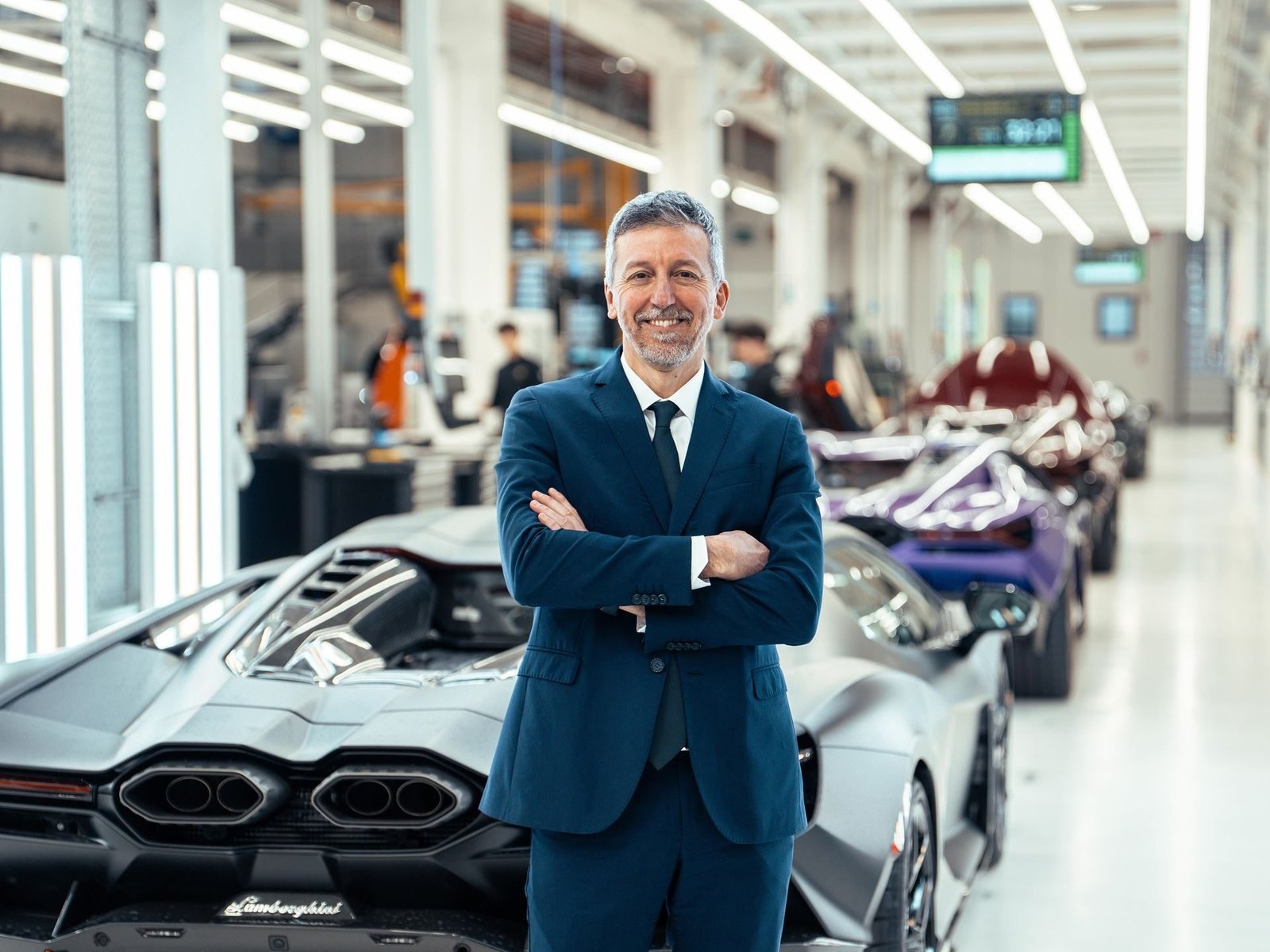 Andrea Costantini, Lamborghini's new Quality Director, standing in the factory with Lamborghini vehicles in production behind him