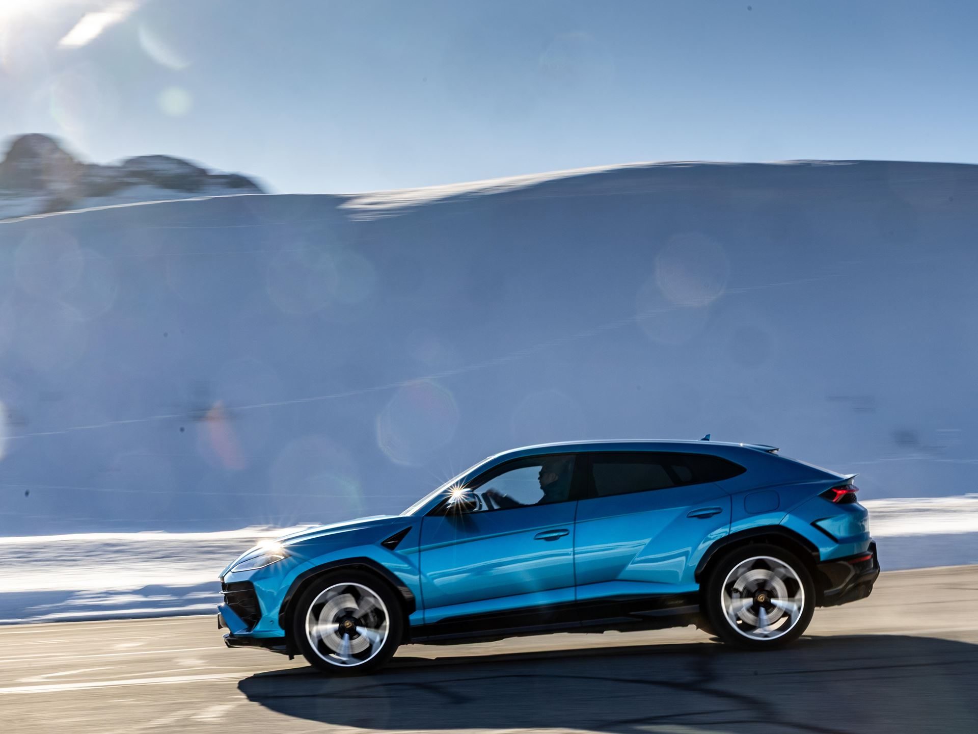 Lamborghini Took Its Hybrid Lineup To The French Alps, And The Convoy Included A Surprise Guest 3 Blue lamborghini urus se driving on a snowy mountain road with sun flare and motion blur