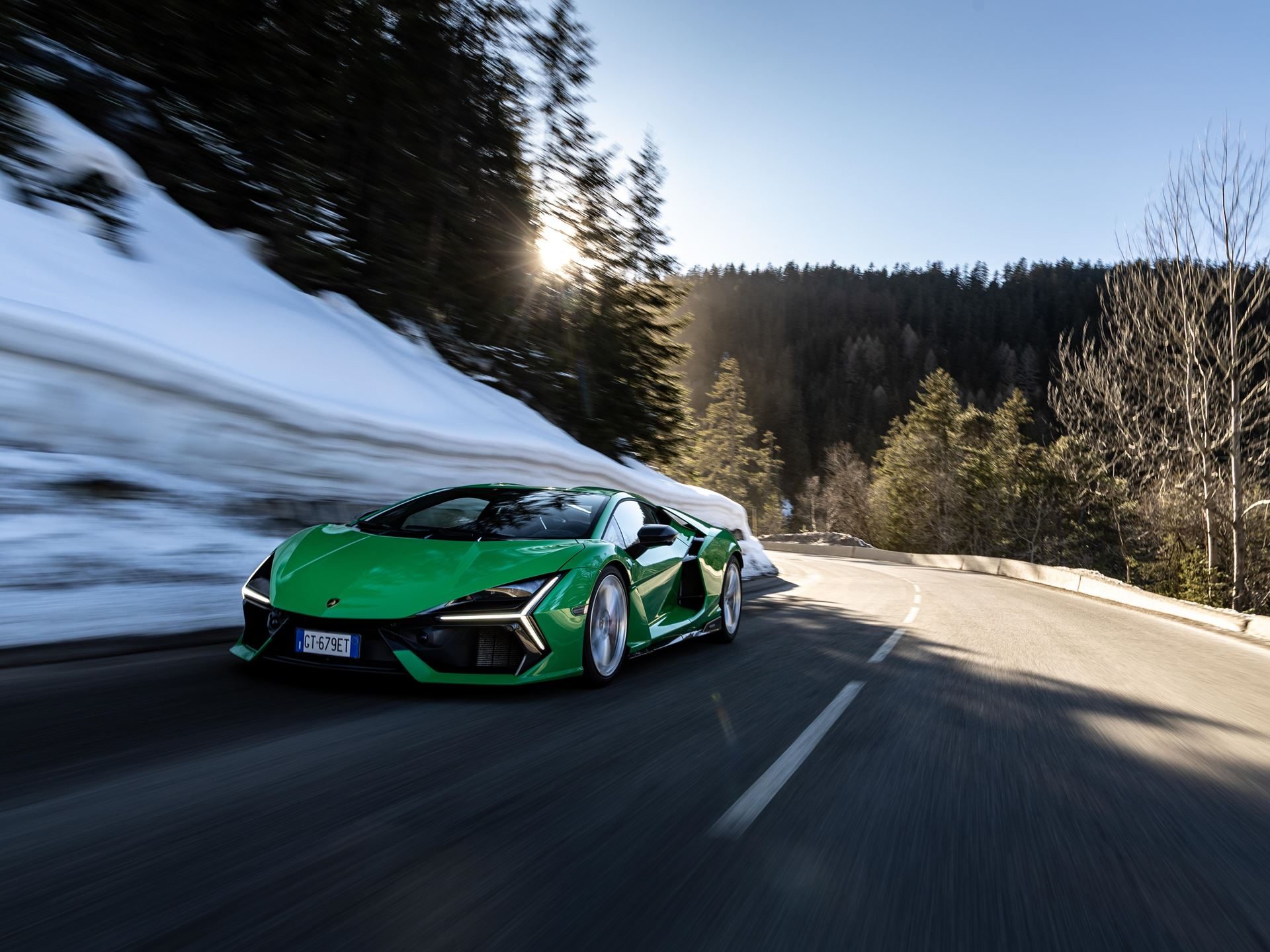 Lamborghini Took Its Hybrid Lineup To The French Alps, And The Convoy Included A Surprise Guest 5 Green lamborghini revuelto driving dynamically on a winding road through a snowy forest with sunlight filtering through trees