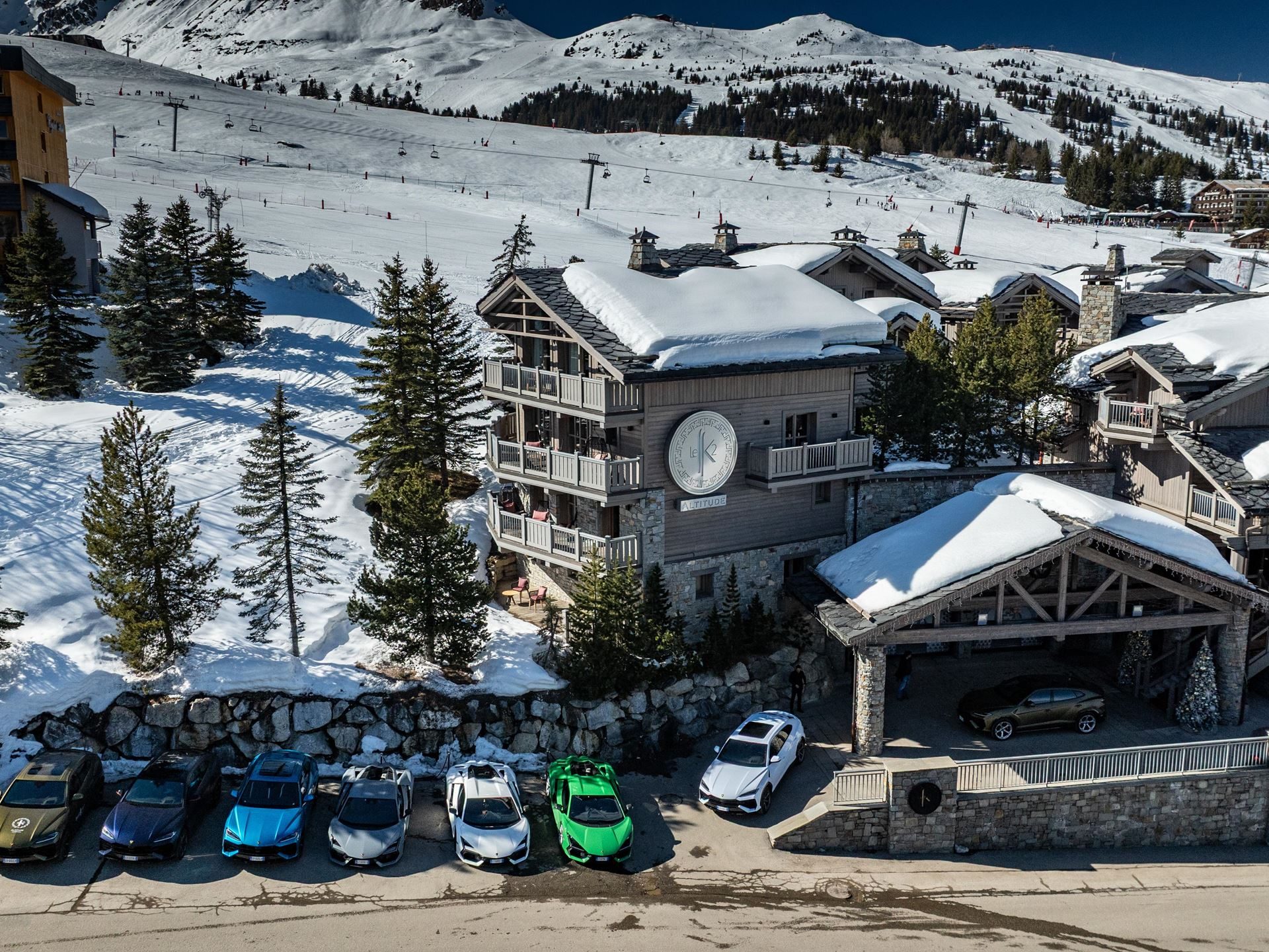Lamborghini Took Its Hybrid Lineup To The French Alps, And The Convoy Included A Surprise Guest 9 Aerial view of multiple lamborghini models parked in front of a luxurious ski chalet at a snowy resort with ski slopes behind