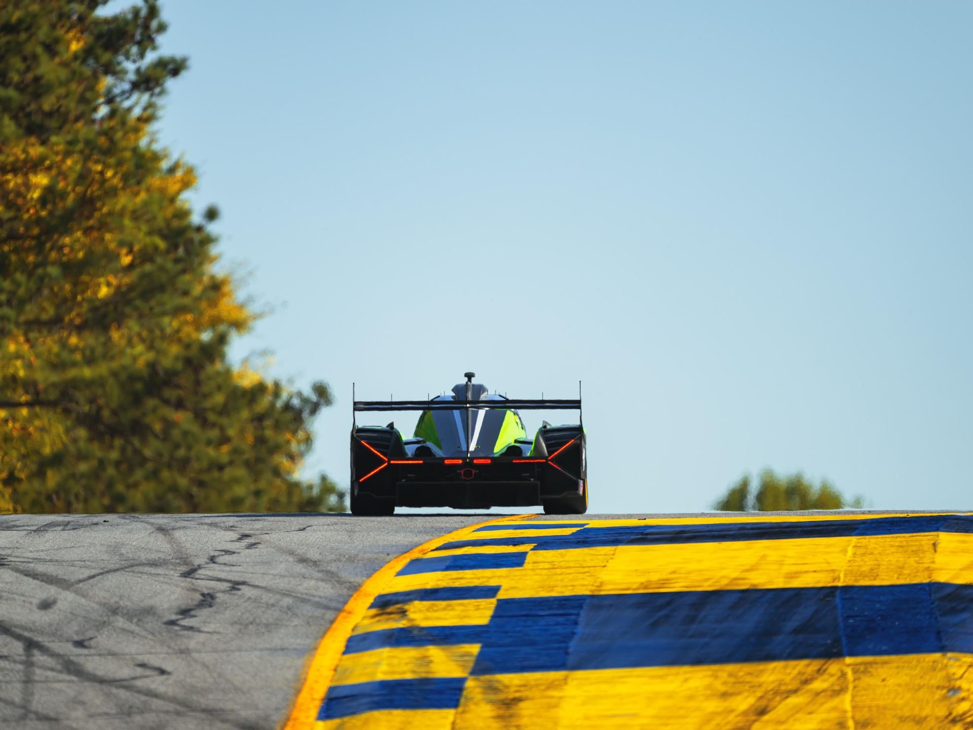 Kvyat Rejoins Grosjean And Mortara As The Lamborghini Sc63 Heads To Its Last Imsa Gtp Start 5 Rear view of the lamborghini sc63 climbing a hill on a racetrack with yellow and blue curbing, showing its large rear wing and diffuser