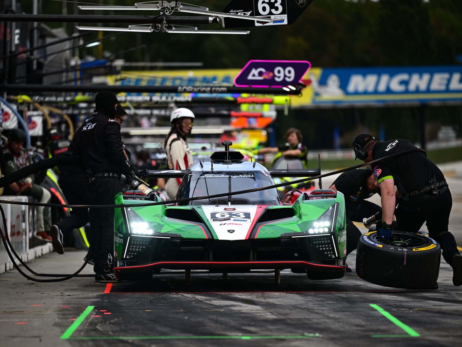 The lamborghini sc63 in the pit lane during a tire change with pit crew members actively working on the car