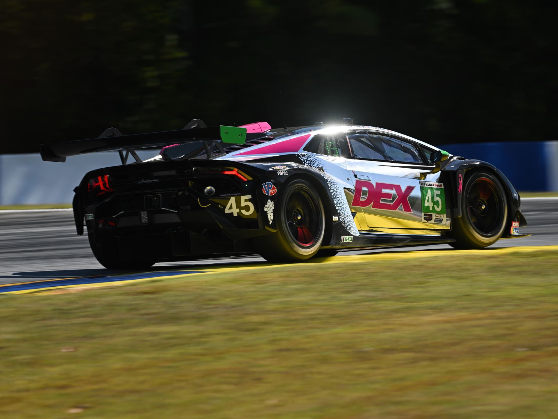 A lamborghini huracán gt3 evo2 race car with pink and green accents speeds around a corner at road atlanta