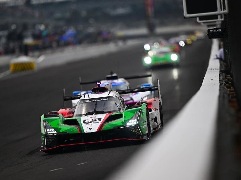 Lamborghini SC63 number 63 racing at night on a wet track in green, red, and white livery at Indianapolis Motor Speedway