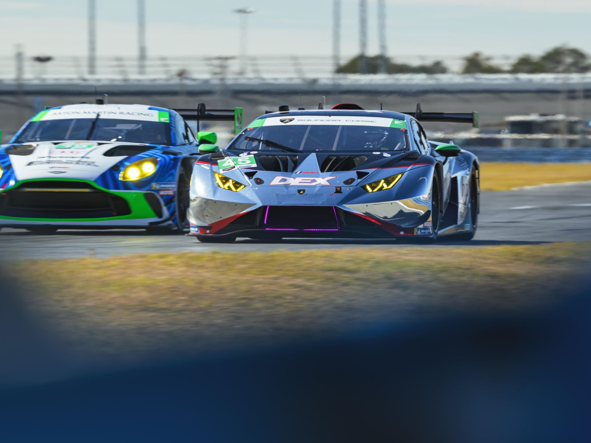 Lamborghini Sc63 Returns To Sebring Seeking Redemption After Daytona Retirement 7 A grey lamborghini huracán gt3 evo2 with purple accents racing alongside an aston martin racing car
