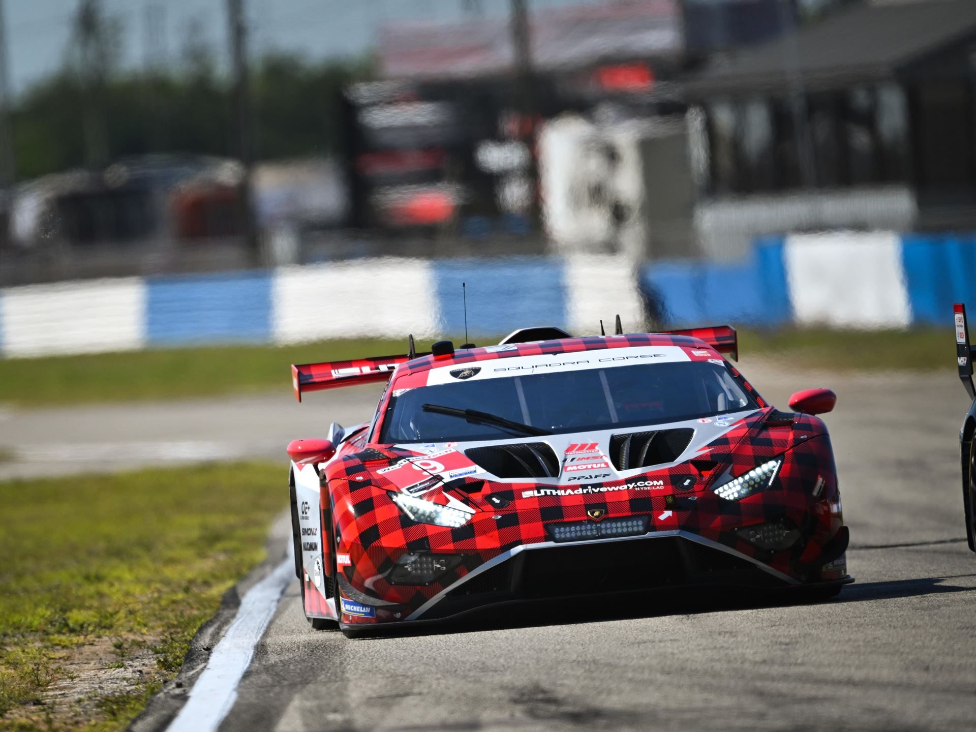 Red and black plaid-liveried lamborghini huracán gt3 evo race car approaching on track with headlights on