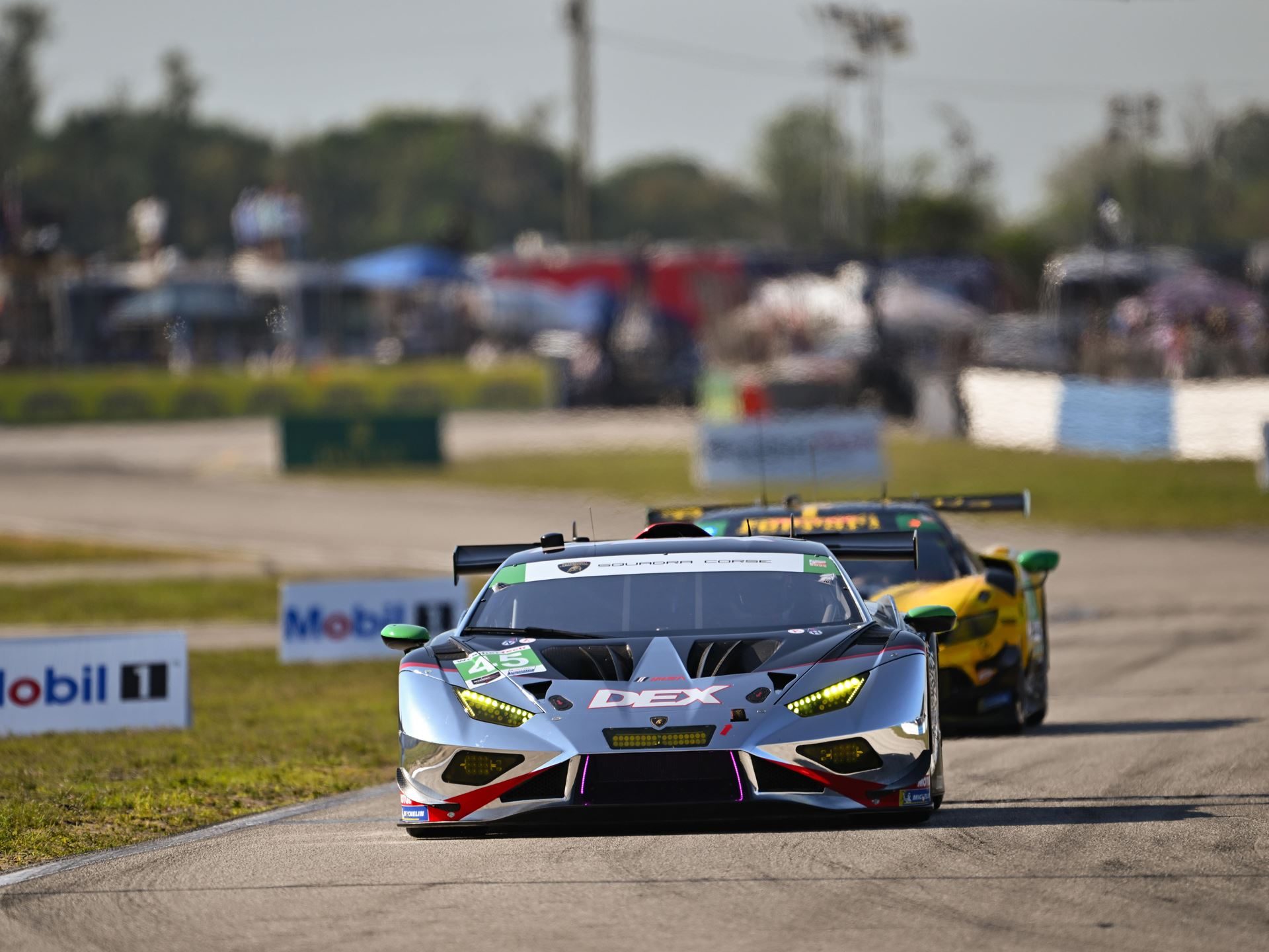 Silver lamborghini huracán gt3 evo number 45 leading another car on a racetrack under bright skies