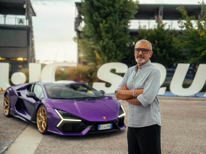 Aldo Drudi stands with arms crossed in front of a purple Lamborghini Revuelto with SUPER TROFEO lettering in the background