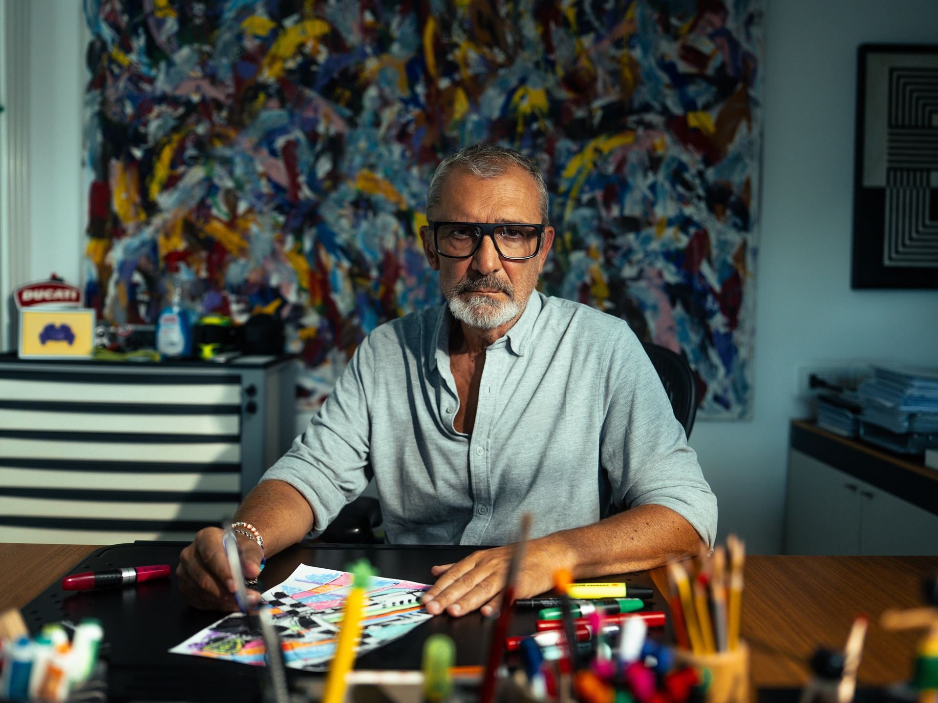 Why Lamborghini Puts The Revuelto Front And Center At Its Biggest Racing Weekend 3 Aldo drudi sits at his desk surrounded by colorful markers and a drawing, with a vibrant abstract painting on the wall behind him