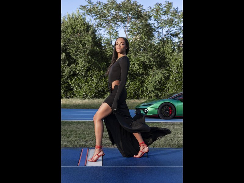 Green Lamborghini Temerario on a blue running track with Italian long jumper Larissa Iapichino posing in a black dress and red heels