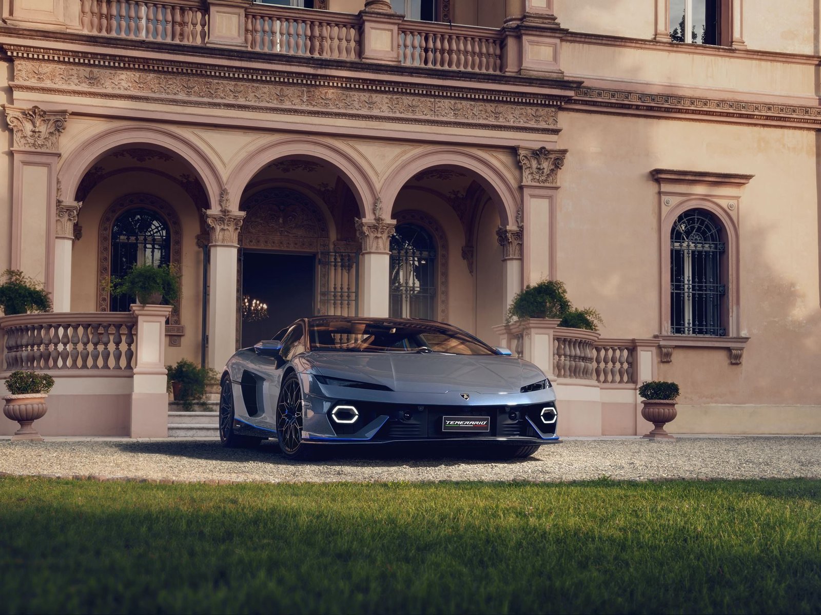 Front view of the Lamborghini Temerario Ad Personam Porto Cervo in Grigio Serget grey with blue accents, parked on a gravel driveway