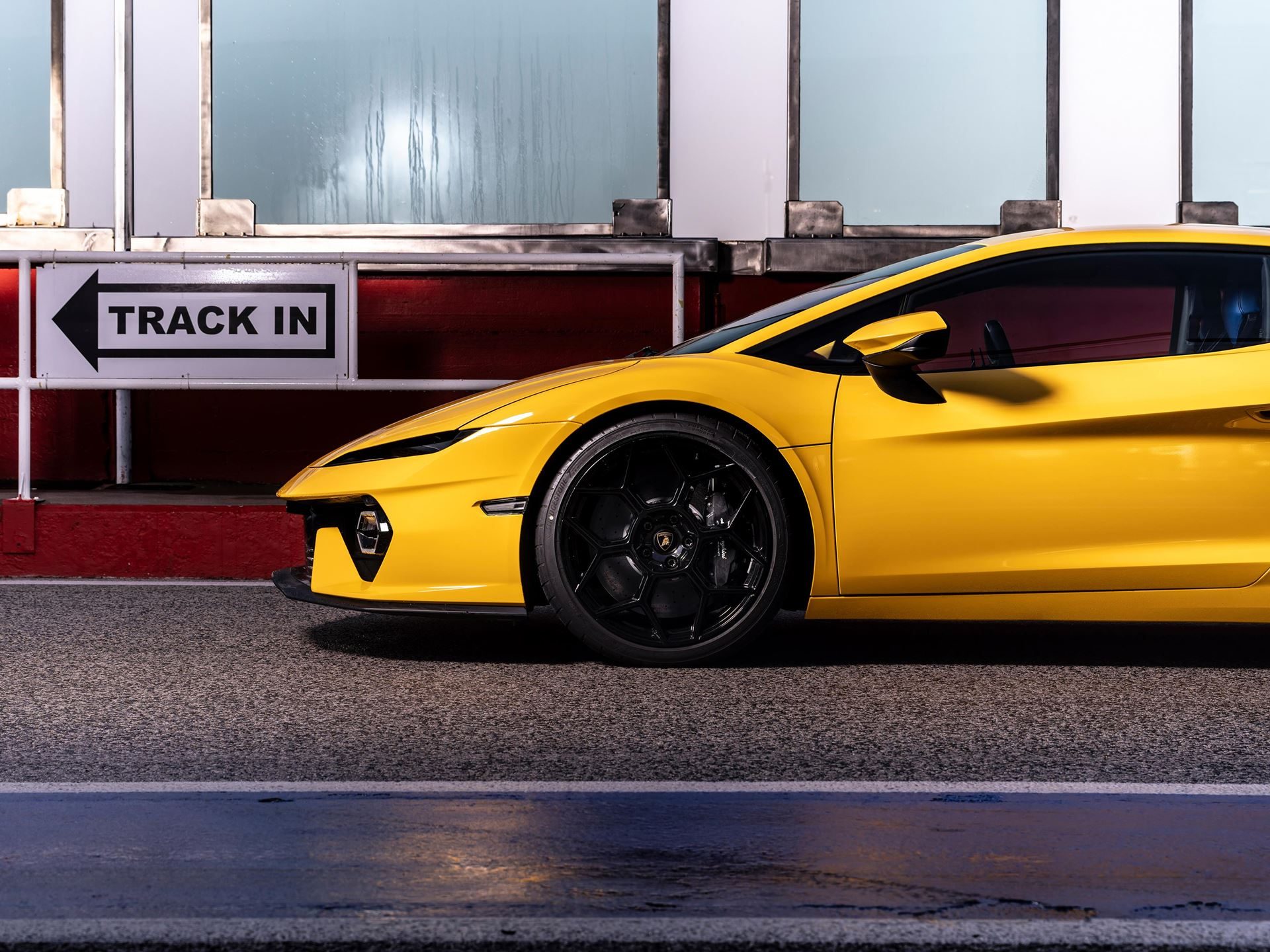 Side view of yellow lamborghini temerario front section near a track in sign showing front splitter and side air intake