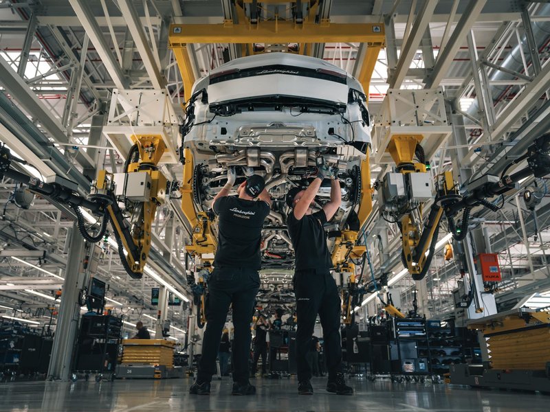 Two Lamborghini production workers assembling the underside of a white Urus on the factory line at Sant'Agata Bolognese