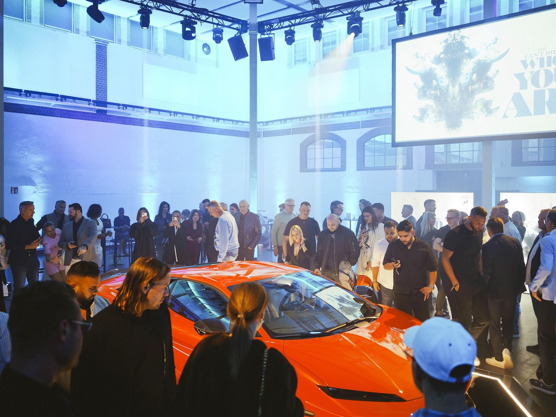 Lamborghini'S 4,000-Kilometer Temerario Tour Reveals How Seriously Sant'Agata Takes Germany 5 Crowd of attendees surrounding the orange lamborghini temerario at an indoor roadshow event