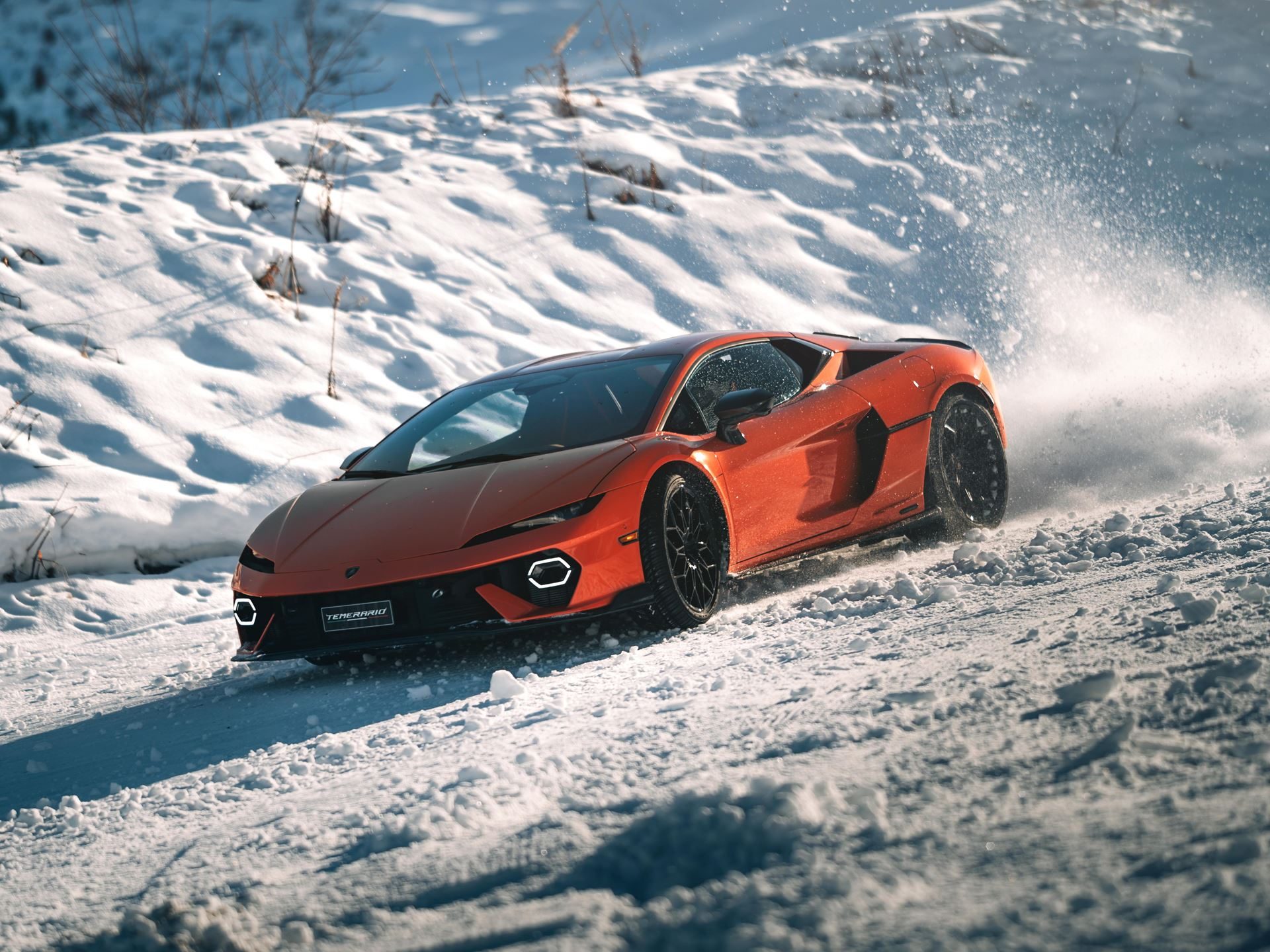 Lamborghini'S Temerario Drifts On Alpine Ice, Proving Its Hybrid System Works Where Grip Doesn'T 3 Orange lamborghini temerario drifting on a snow-covered alpine road with snow spray