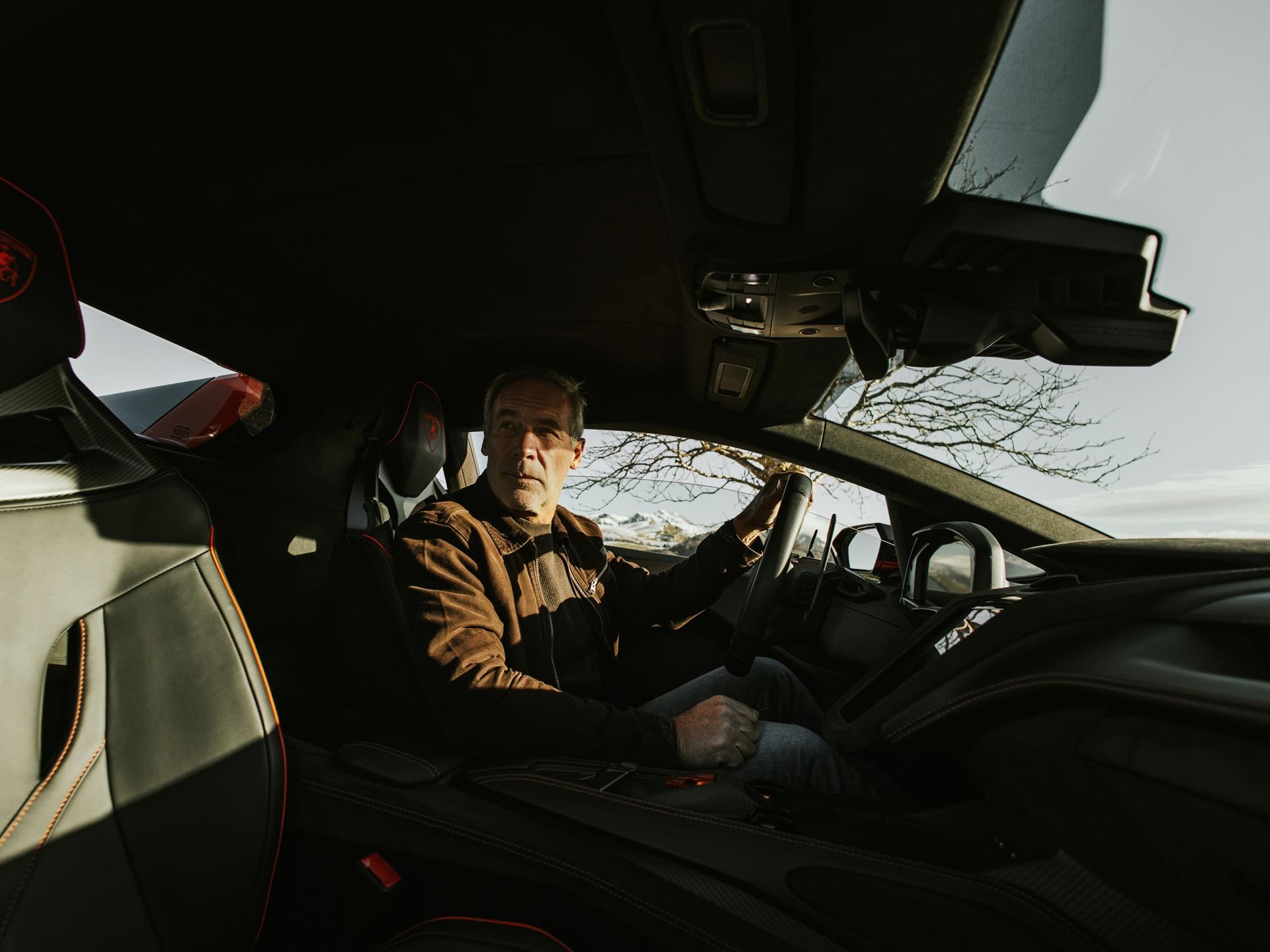 Mike horn seated in the driver's seat of an orange lamborghini temerario, interior showing black and orange accents and modern dashboard