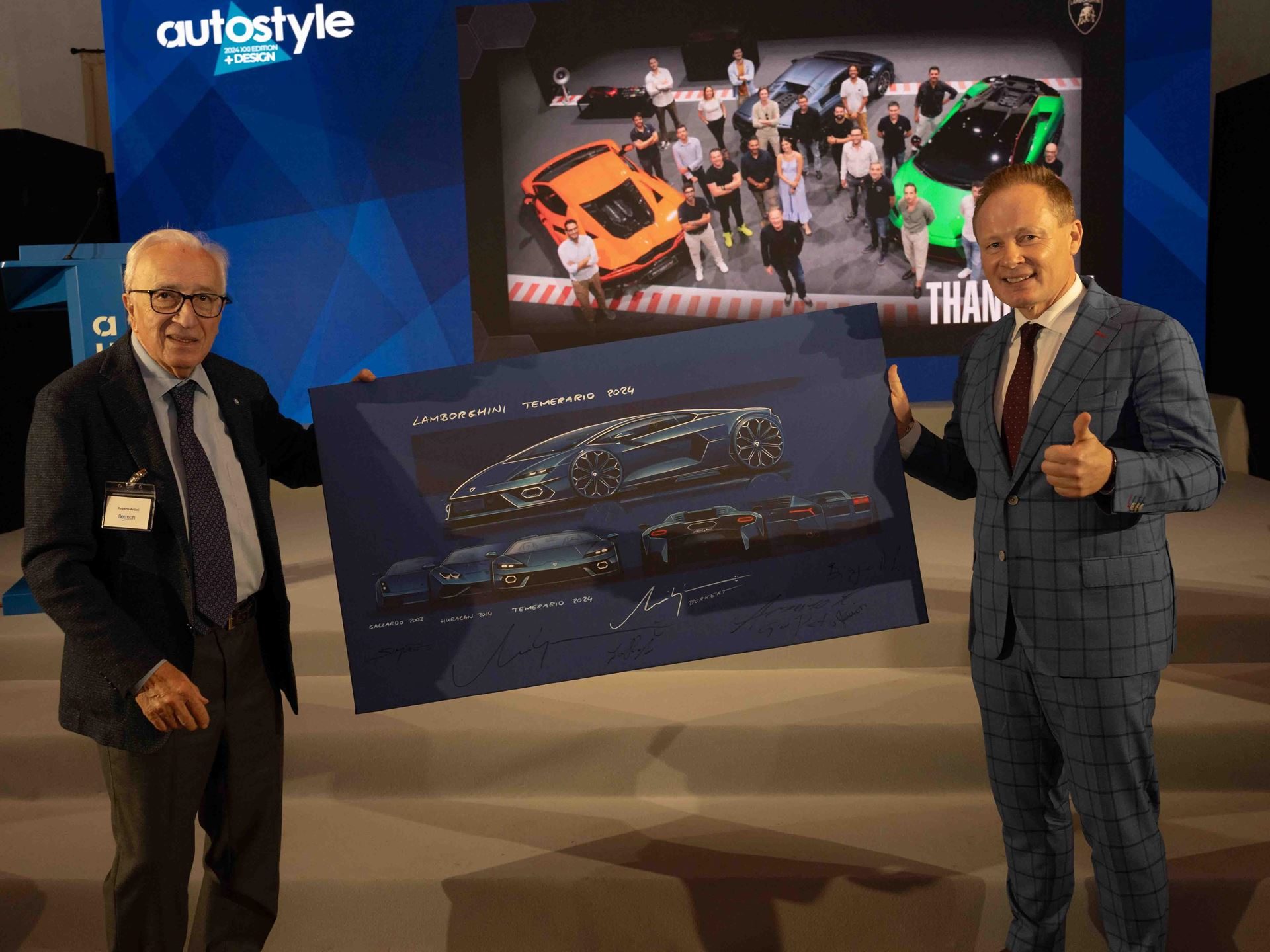 Two presenters holding a lamborghini temerario 2026 design sketch at the autostyle design event with a 3d rendering on screen behind them