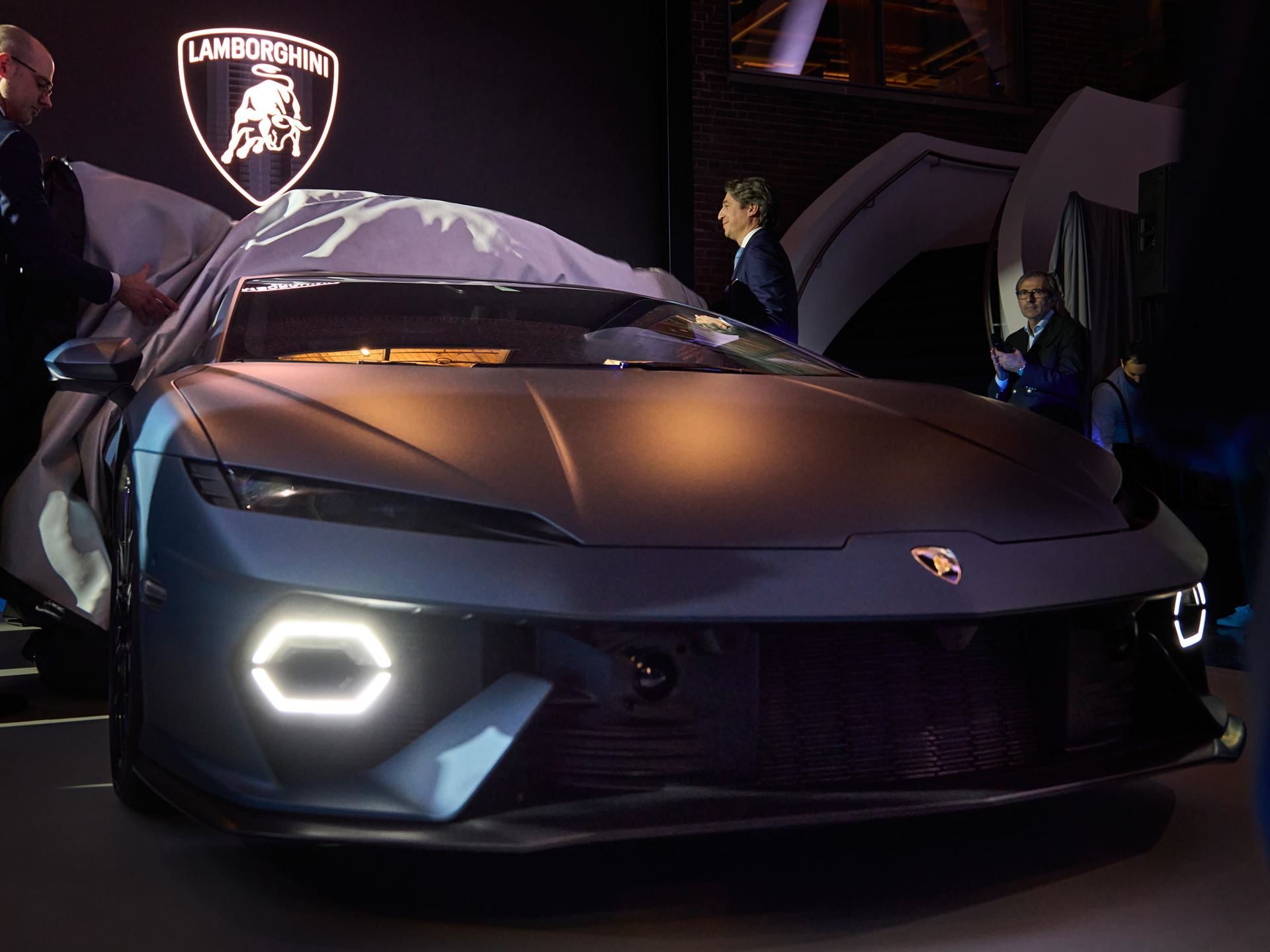 The Lamborghini Temerario being unveiled in Toronto with its cover pulled back revealing hexagonal DRLs and Lamborghini badge