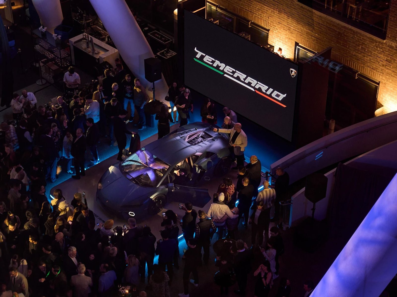 Overhead view of the Lamborghini Temerario debut event in Toronto with the car on an illuminated platform surrounded by attendees