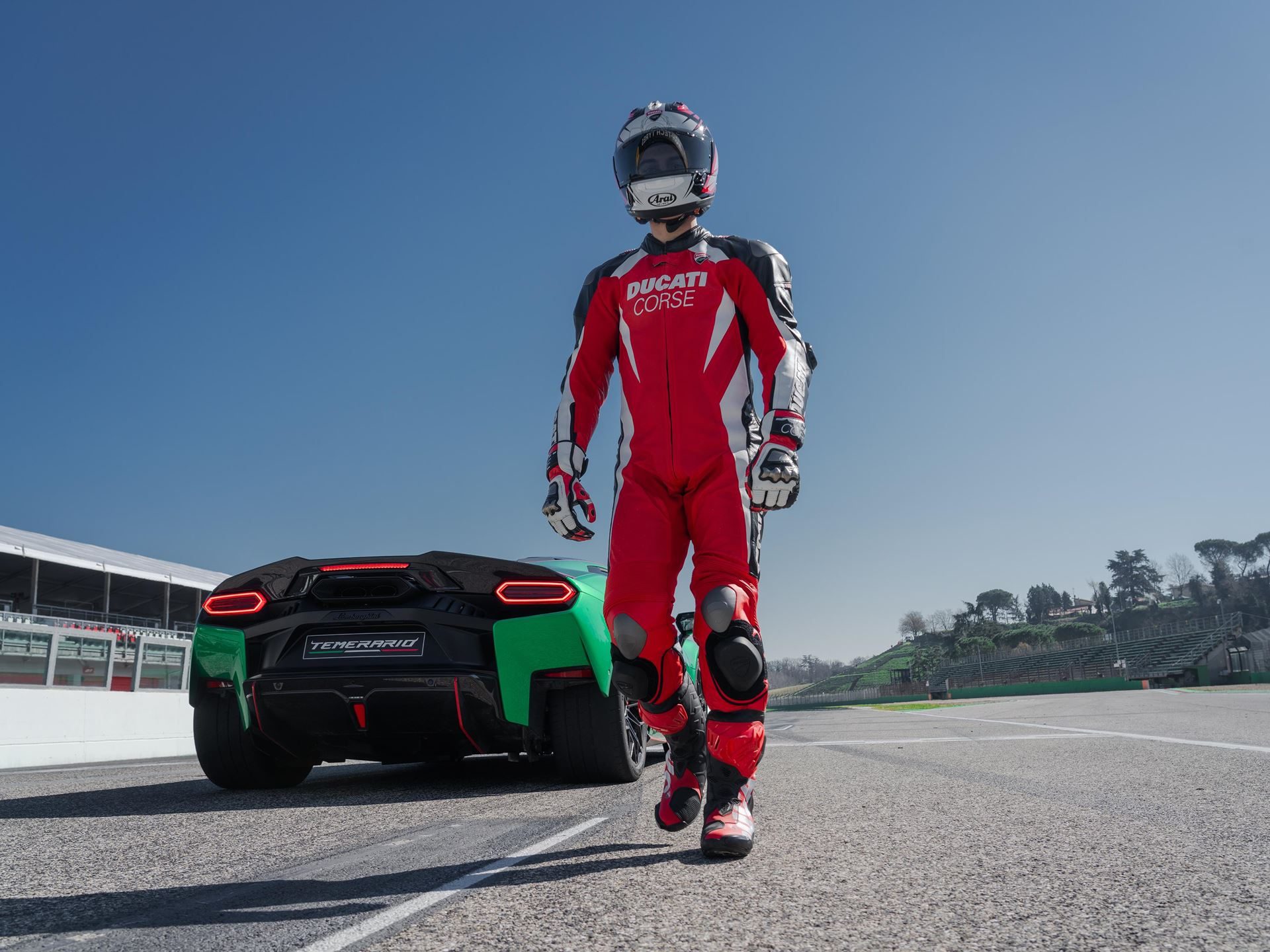 Lamborghini Temerario Takes On Ducati'S Panigale V4 At Imola, And The 10,000 Rpm V8 Does The Talking 9 Ducati rider in red and white racing gear walking away from a green lamborghini temerario parked on the imola circuit