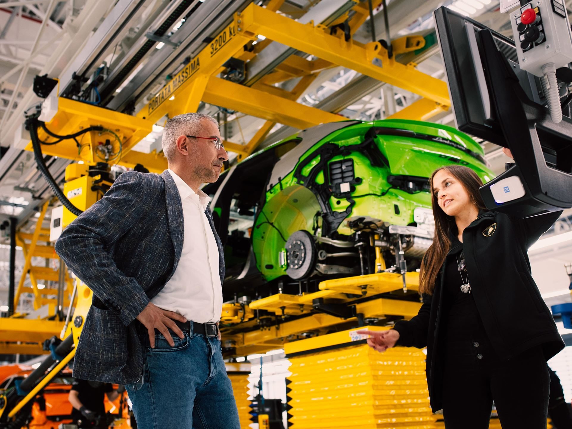 Lamborghini'S 12Th Consecutive Top Employer Award Reveals The Factory Floor Culture Behind Its Supercars 7 Two lamborghini employees discussing production progress with a neon green urus body shell on an overhead conveyor system in the background