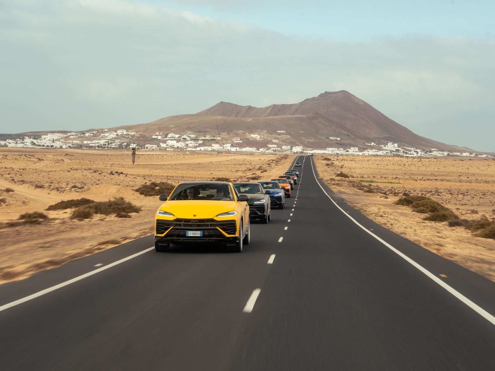 Lanzarote'S Volcanic Terrain Becomes The Proving Ground For Lamborghini'S Plug-In Hybrid Urus Se 7 A convoy of lamborghini urus suvs in yellow, blue, and black driving on a straight road through lanzarote's volcanic landscape