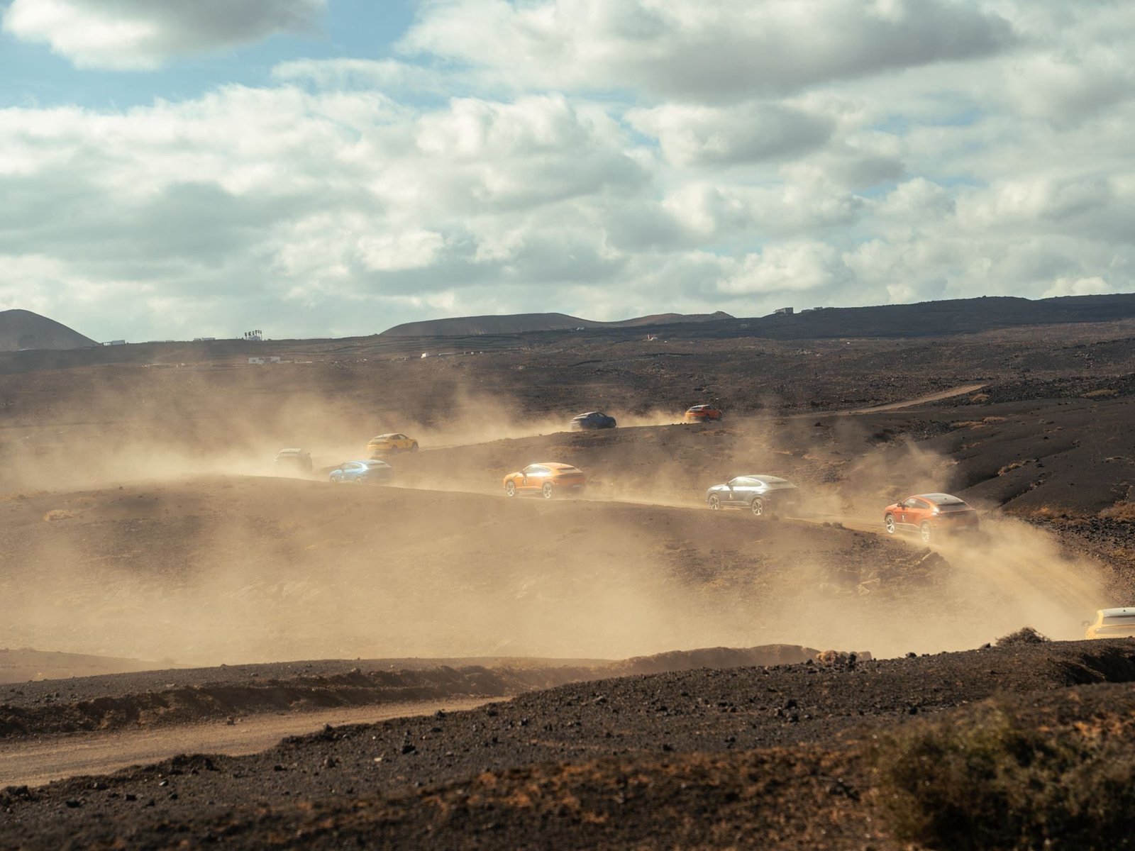 A convoy of colorful Lamborghini Urus SE SUVs kicking up dust on a volcanic dirt track in Lanzarote