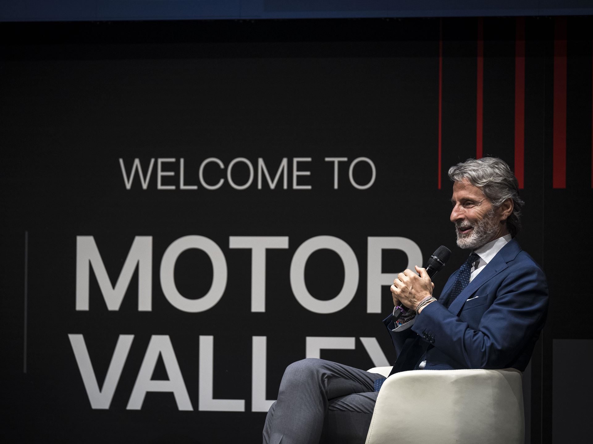Lamborghini'S Urus Se 'Tettonero' Capsule Turns Motor Valley Fest Into A Masterclass In Bespoke Hybrid Luxury 5 Stephan winkelmann in a blue suit holding a microphone on stage at motor valley fest with welcome to motor valley graphic behind him