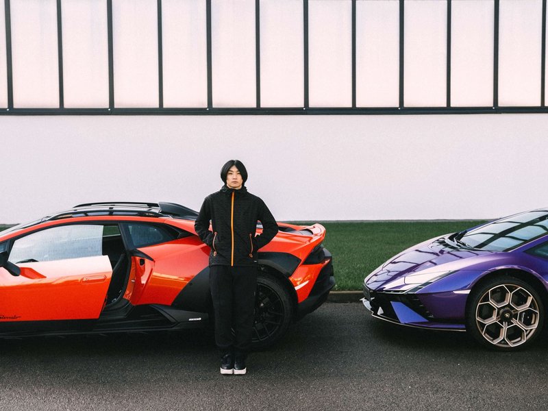 Model in black and orange Macron Lamborghini activewear standing between an orange Huracan Sterrato and a purple Huracan Tecnica