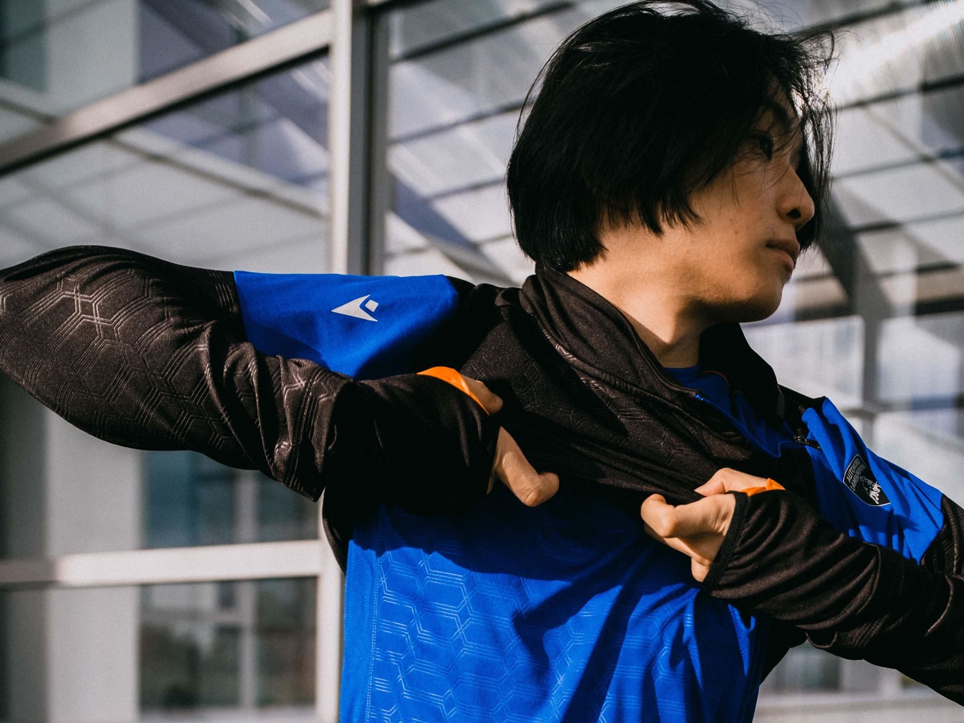 Lamborghini'S Second Macron Activewear Drop Stitches Car-Seat Hexagons Into Running Gear 3 Close-up of model adjusting black and blue activewear jacket showing subtle geometric hexagonal pattern on the fabric