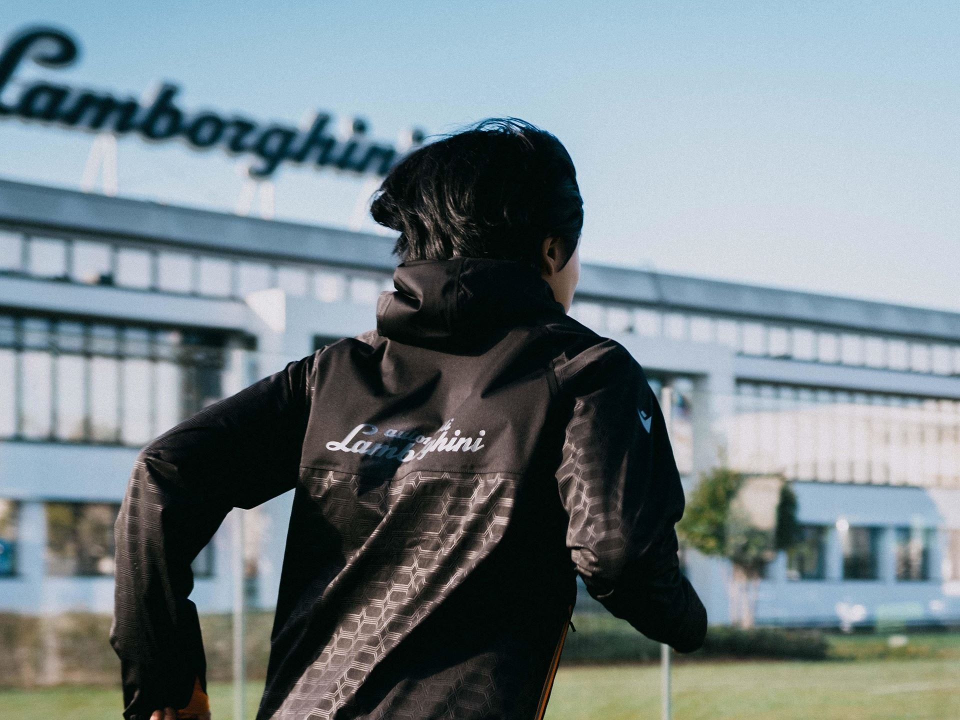 Lamborghini'S Second Macron Activewear Drop Stitches Car-Seat Hexagons Into Running Gear 7 Person in lamborghini-branded activewear running with the lamborghini factory building in sant'agata bolognese visible in the background