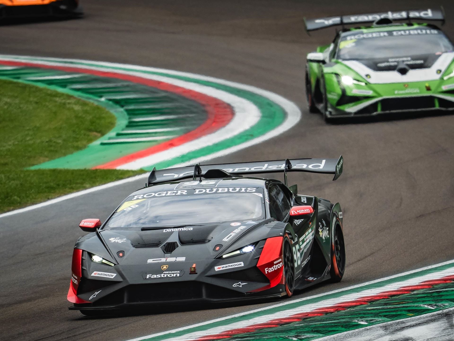 A black and red #86 huracán super trofeo evo2 leads a green lamborghini through a corner at imola with red and white curbing visible