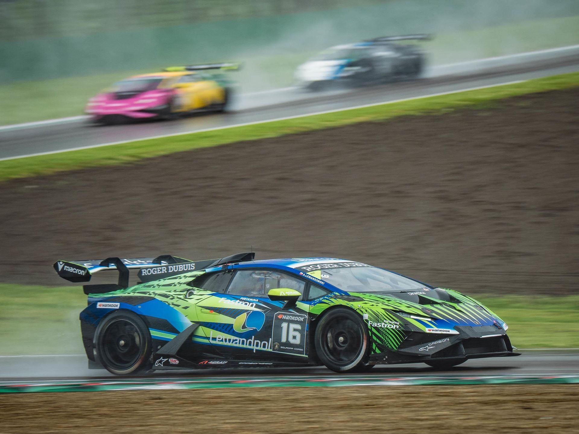 A green and blue #16 huracán super trofeo evo2 kicks up spray on the wet imola circuit during race 2