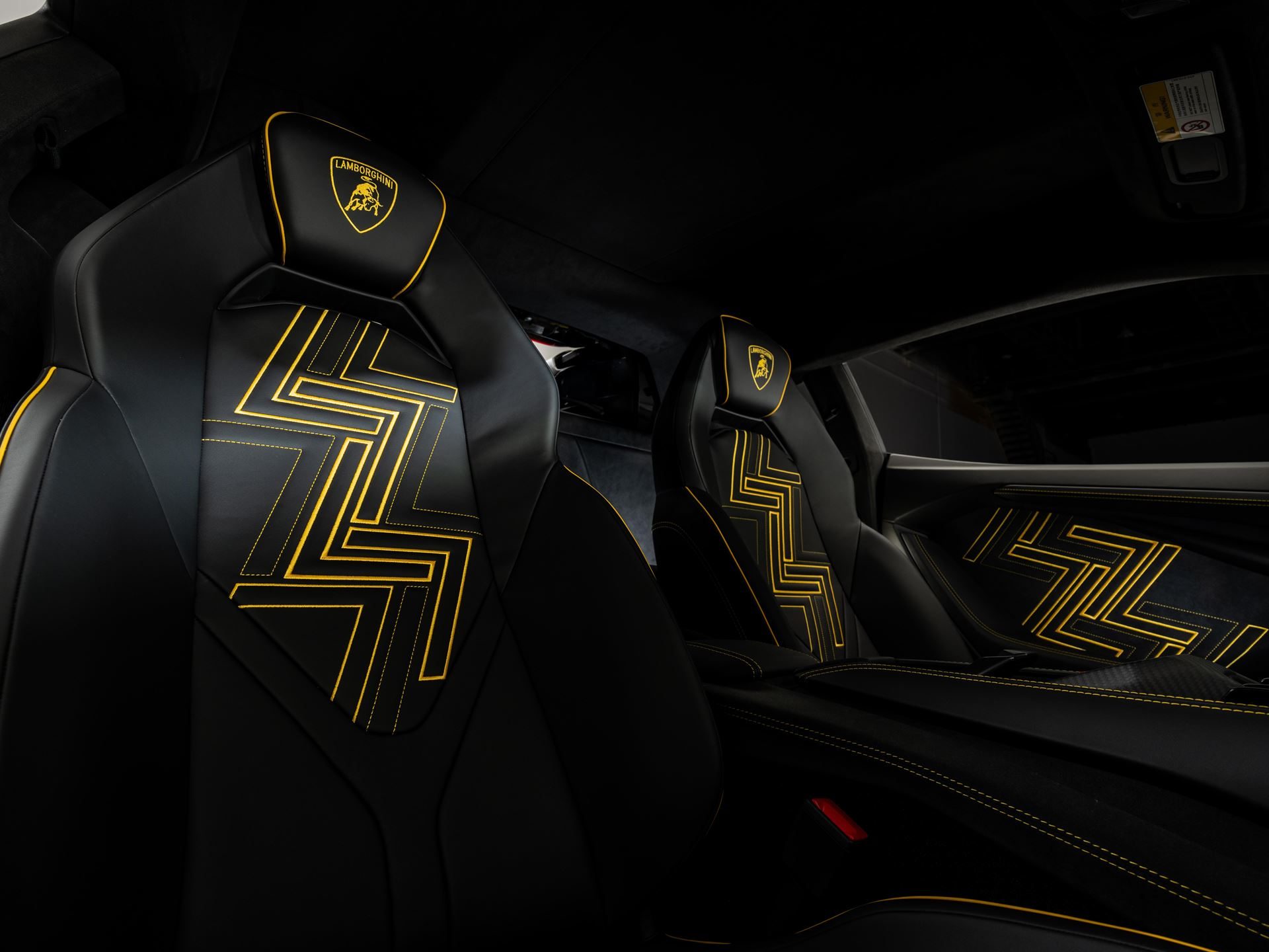 Close-up of black leather seats with yellow geometric stitching, l monogram pattern, and lamborghini crests on headrests