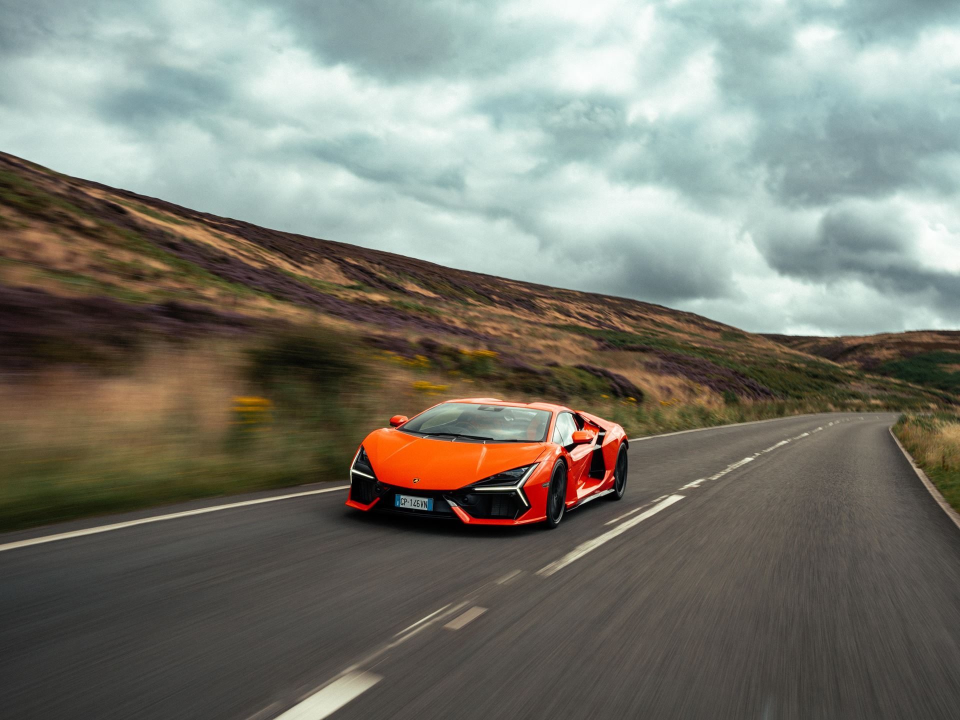 Lamborghini Taps Manchester City'S Rúben Dias To Front Its 1,001-Hp Flagship 3 Orange lamborghini revuelto at speed on a winding rural road with motion blur and dramatic cloudy sky