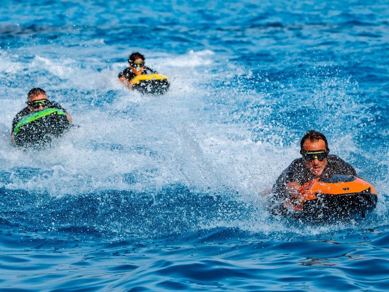 Three riders on Lamborghini-branded SEABOB watercraft cutting through open ocean water