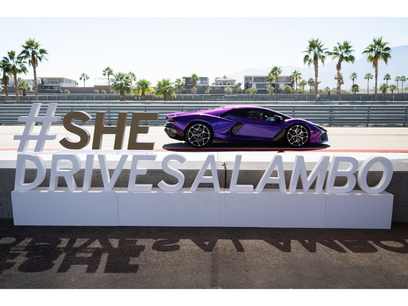 Purple Lamborghini Revuelto parked on the racetrack at The Thermal Club next to a large #SHEDRIVESALAMBO sign with palm trees in the background