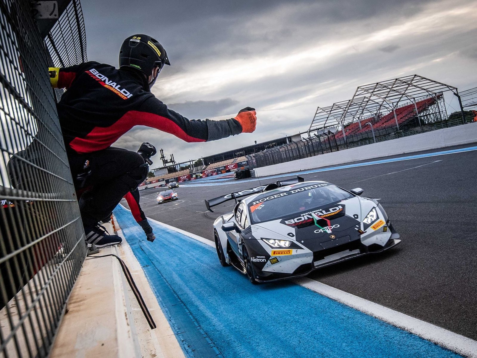 A Lamborghini Huracán Super Trofeo EVO race car speeds past a pit crew member on track at Paul Ricard under cloudy skies