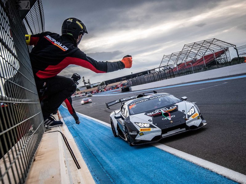 A Lamborghini Huracán Super Trofeo EVO race car speeds past a pit crew member on track at Paul Ricard under cloudy skies