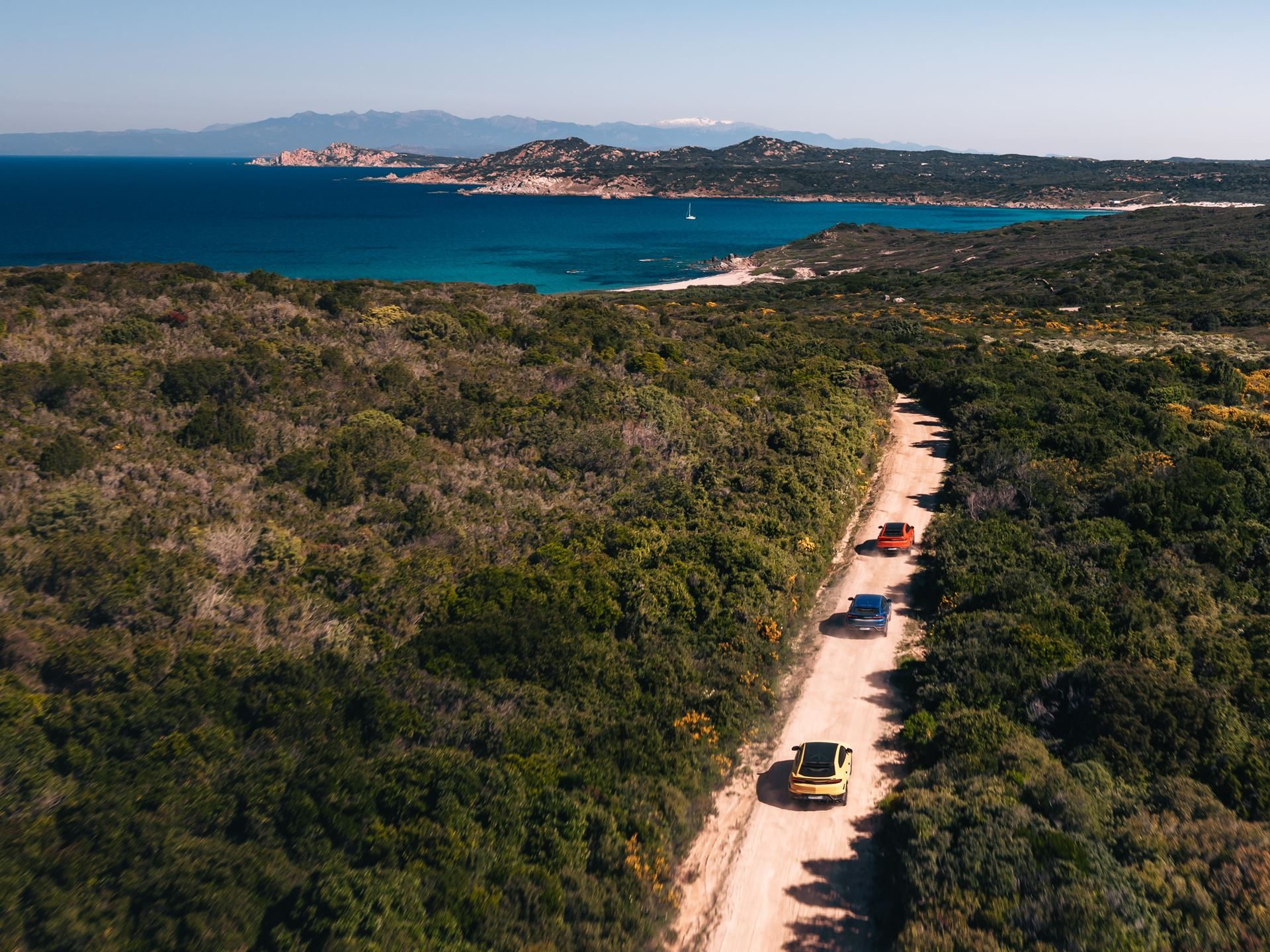The Urus Se Staked Lamborghini'S Hybrid Credibility On Sardinian Dirt 7 Aerial view of three lamborghini urus models driving on a dirt road through green scrubland with the sardinian sea in the background