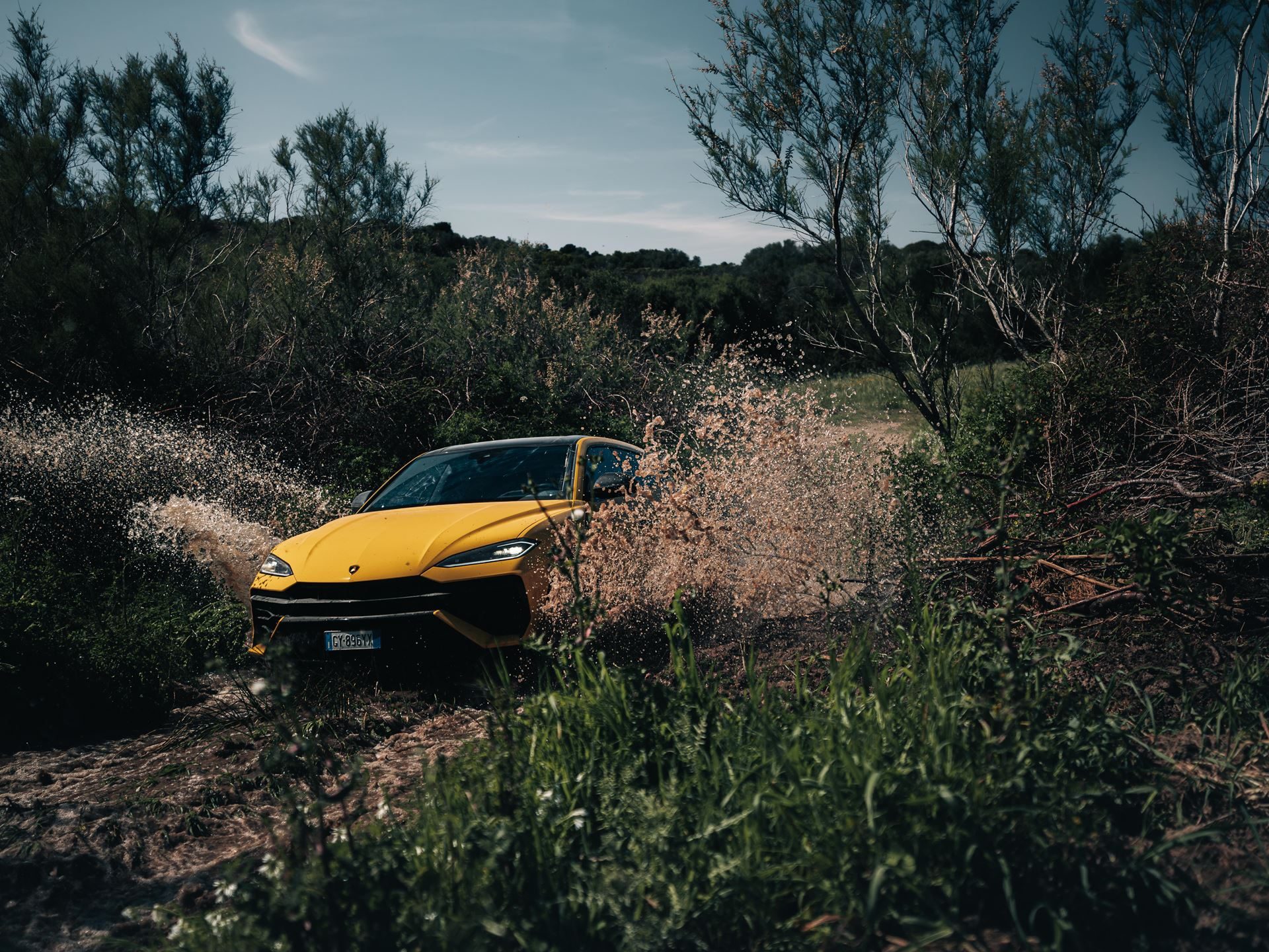 The Urus Se Staked Lamborghini'S Hybrid Credibility On Sardinian Dirt 9 Yellow lamborghini urus splashing through a muddy puddle on an off-road trail surrounded by green vegetation