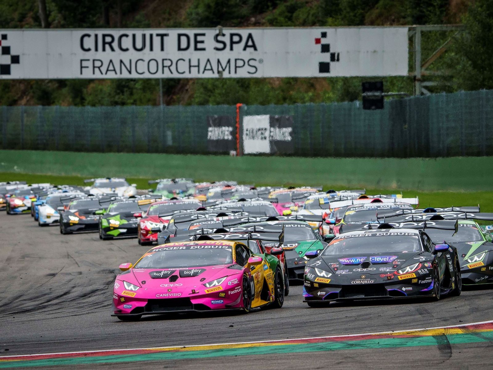 A pack of Lamborghini Huracán Super Trofeo EVO2 race cars in colorful liveries racing through Spa-Francorchamps