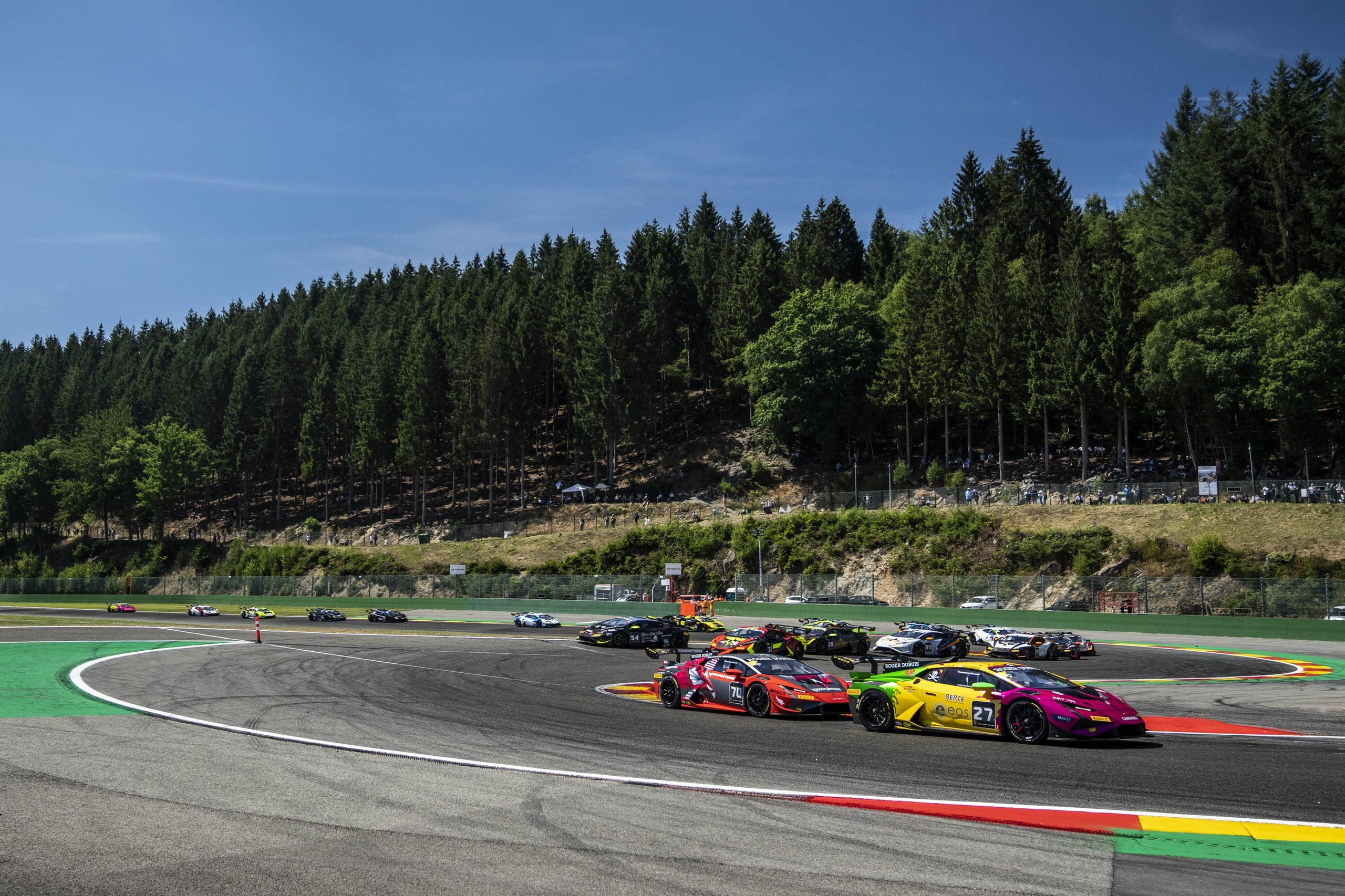 Multiple lamborghini huracán super trofeo evo2 race cars battling through a turn on a forest-lined circuit