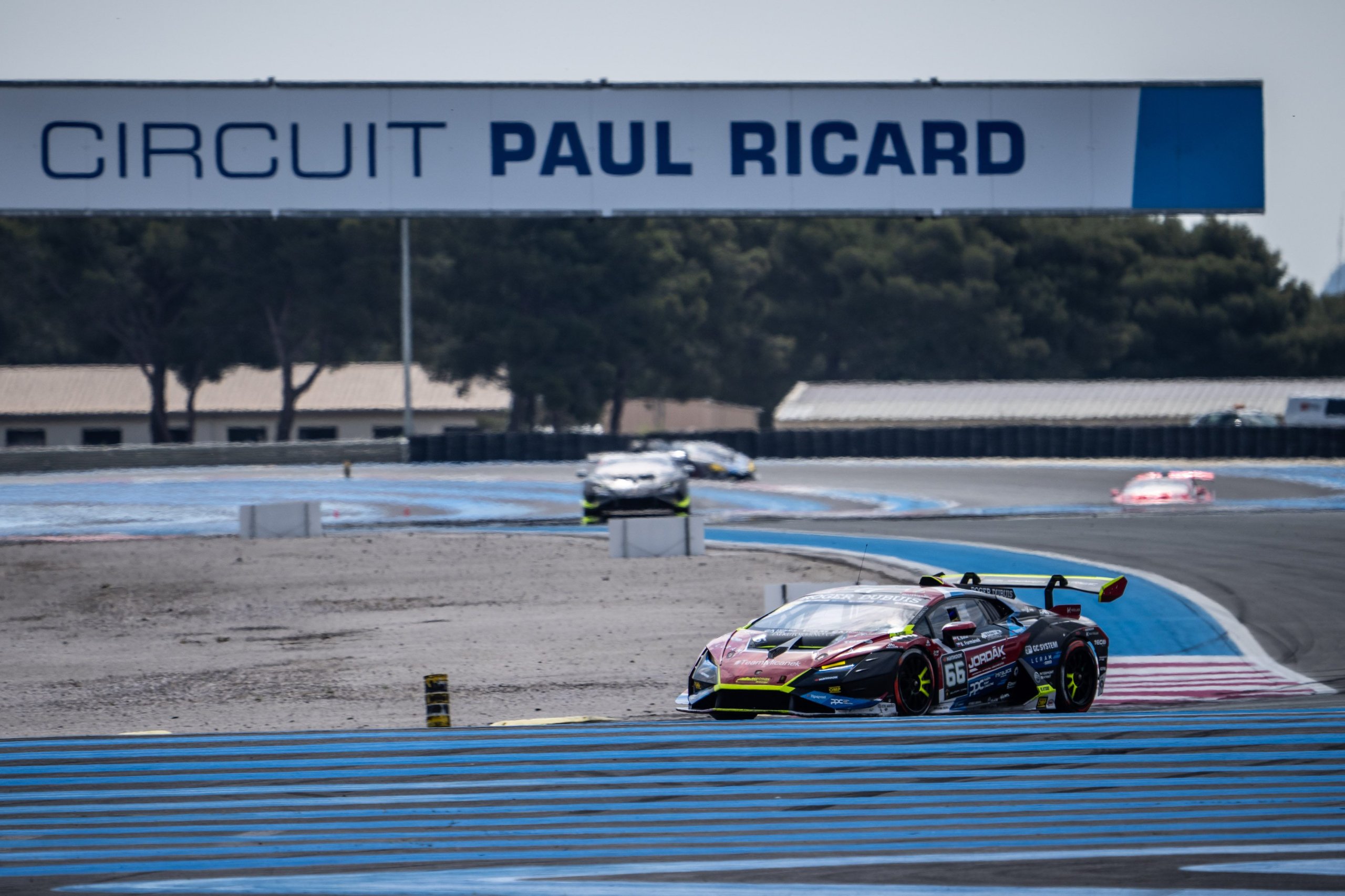 A black and red lamborghini huracán super trofeo evo2 navigates a turn at circuit paul ricard with the circuit sign visible
