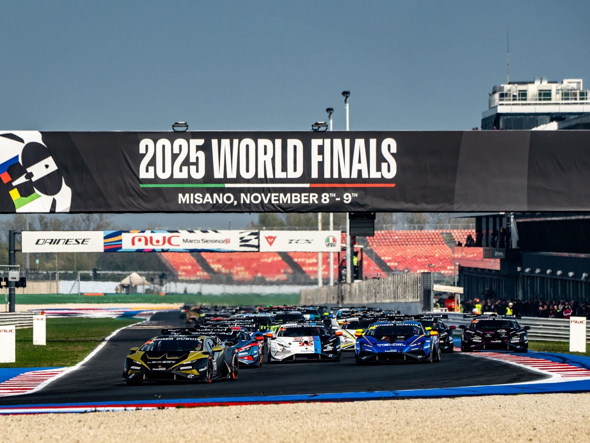 One-Point Margins And Last-Lap Passes: How The 2025 Super Trofeo Season Built The Most Dramatic World Finals In Years 9 Wide shot of lamborghini huracán super trofeo evo2 race cars at the start of a race with 2025 world finals banner overhead and spectators in grandstands
