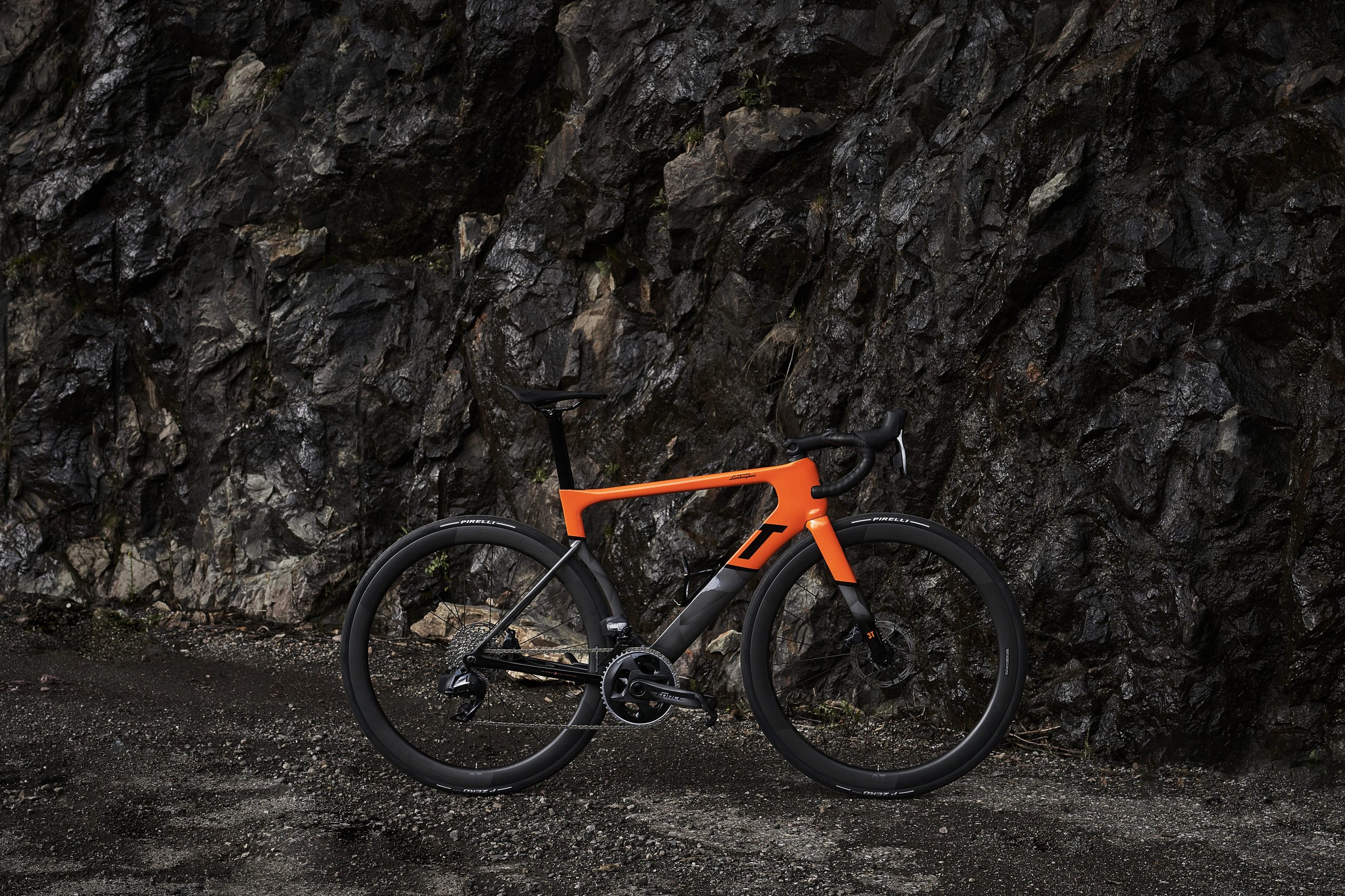 Lamborghini'S Centro Stile Designed Two New 3T Bicycles, And They Cost Less Than A Set Of Revuelto Brake Pads 13 Full side view of the orange arancio apodis 3t racemax x automobili lamborghini gravel bicycle on a dirt road against a dark cliff face