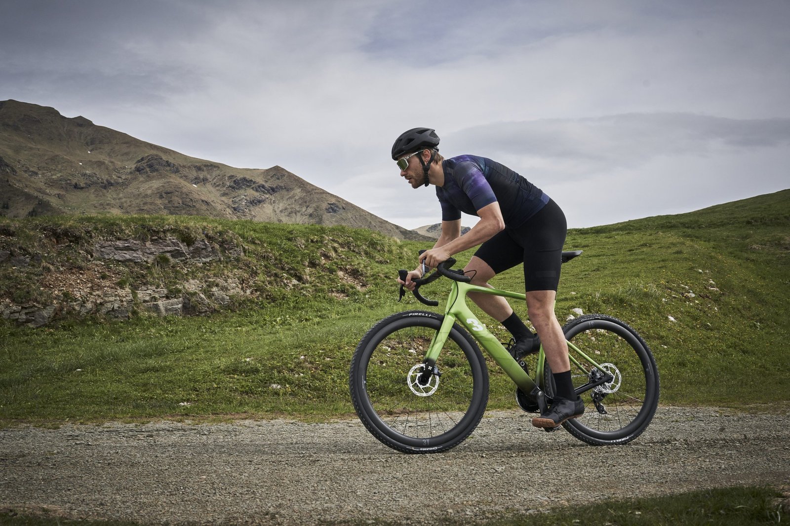 Cyclist riding a green 3T Racemax x Automobili Lamborghini gravel bicycle through a mountainous gravel road landscape