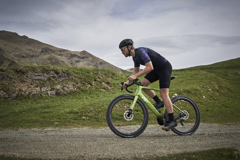 Cyclist riding a green 3T Racemax x Automobili Lamborghini gravel bicycle through a mountainous gravel road landscape