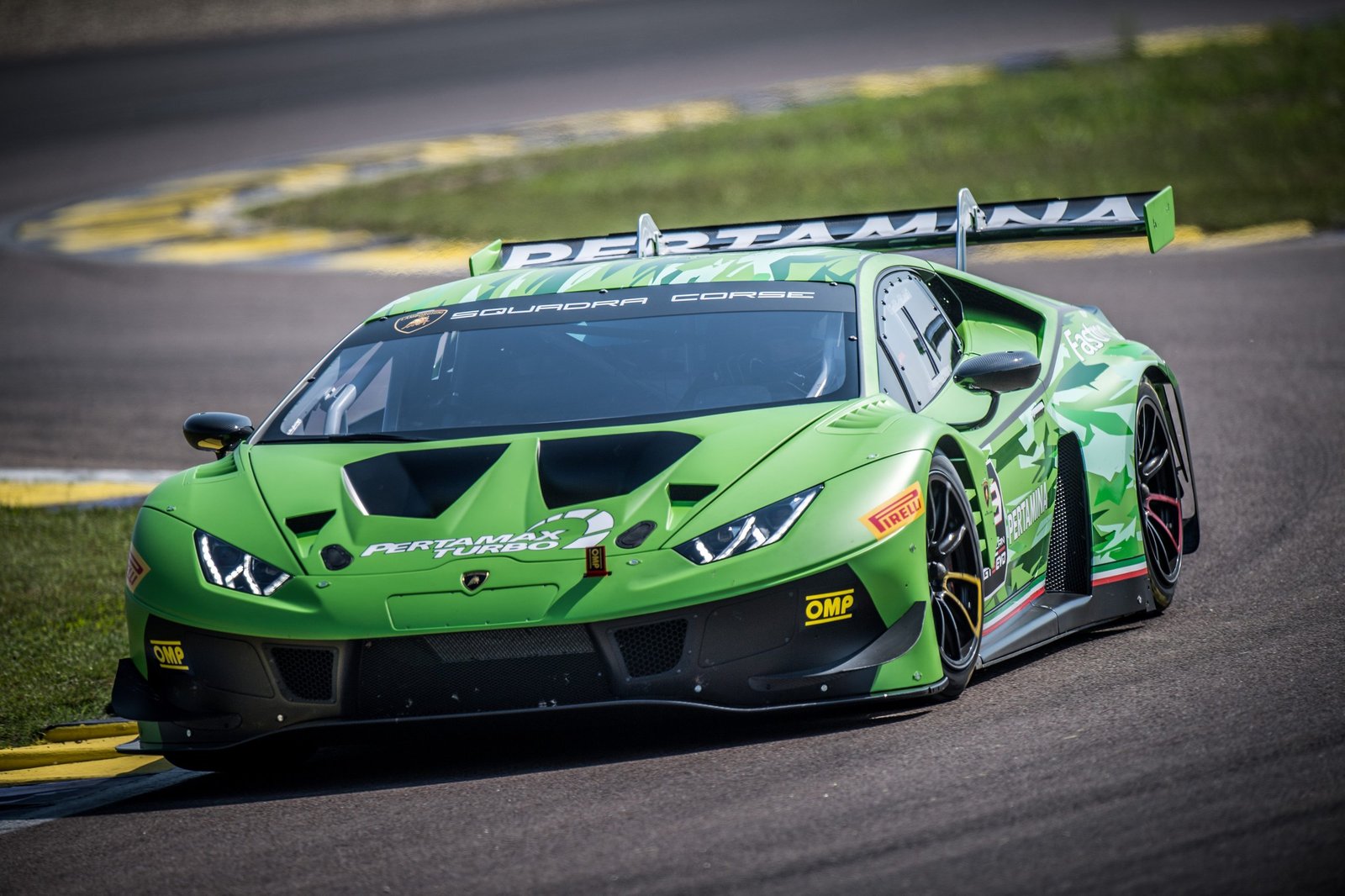 Green Lamborghini Huracán GT3 EVO racing through a corner on a sunlit racetrack with Squadra Corse branding visible on the windshield